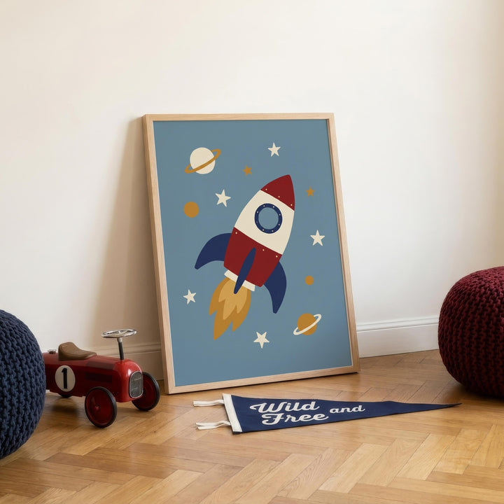 a framed poster of a rocket ship flying through a space scene, accompanied by a toy car and a blue flag with the text "Wild Free and" on it.